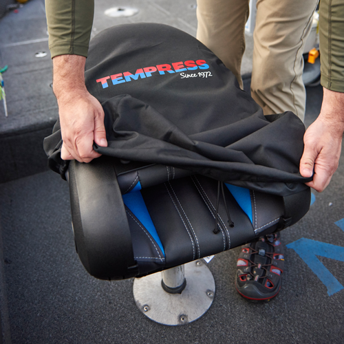 Person holding a black and blue TEMPRESS branded seat cover over a chair.